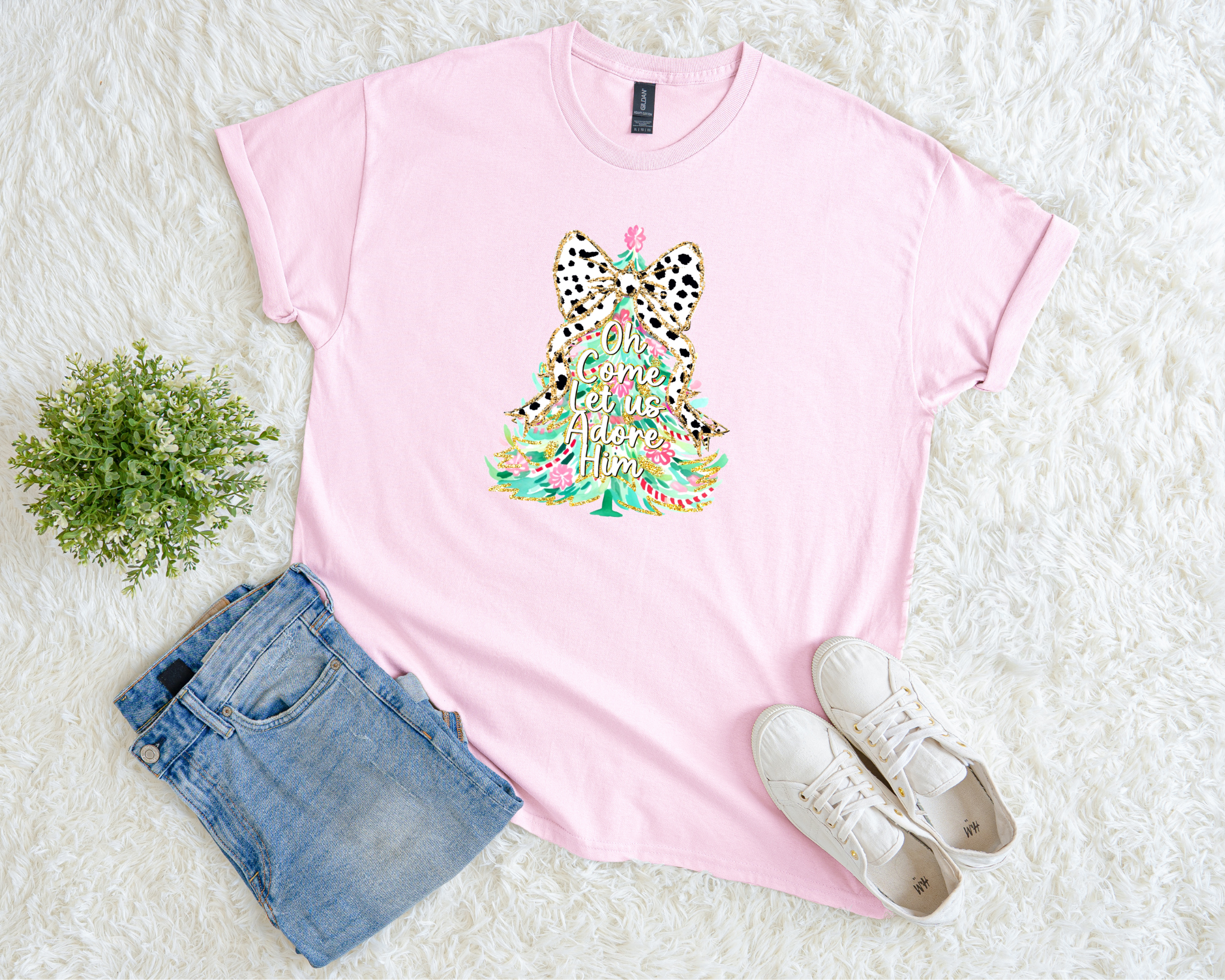pink Christmas t-shirt featuring a colorful tree with a leopard bow and the phrase “Oh Come Let Us Adore Him,” styled flat with jeans and sneakers on a soft white background.