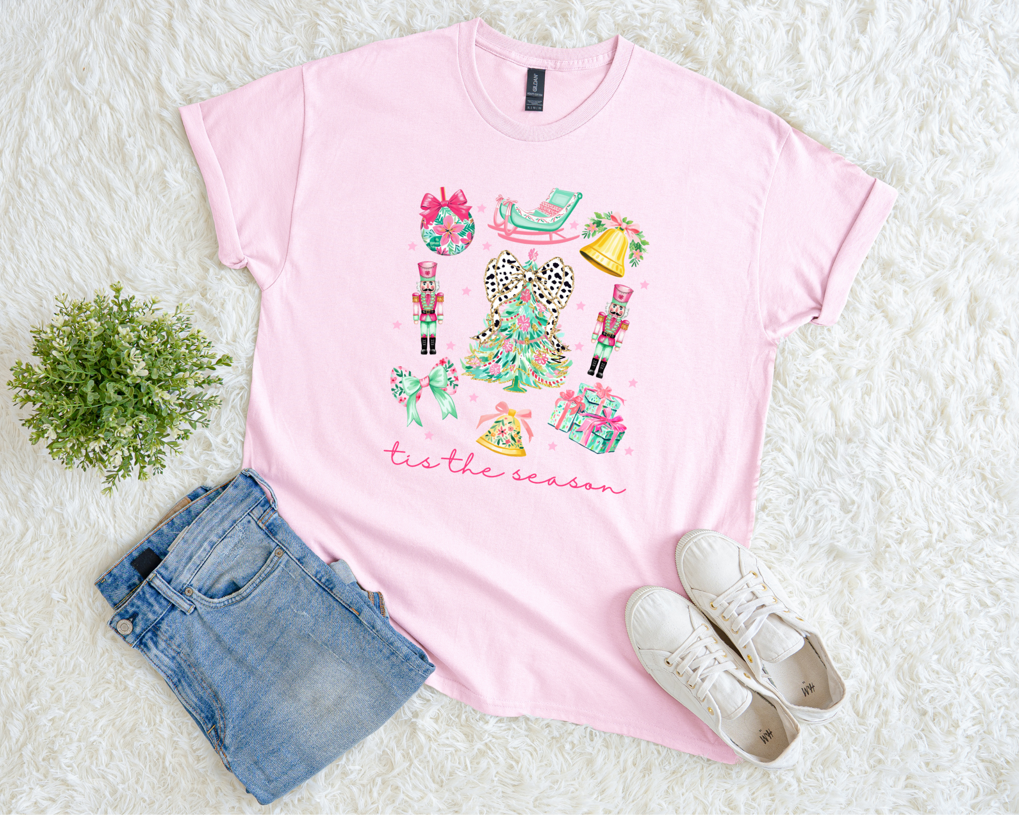 t-shirt featuring a colorful “‘Tis the Season” design with nutcrackers, pastel gifts, bows, and a leopard-bow Christmas tree