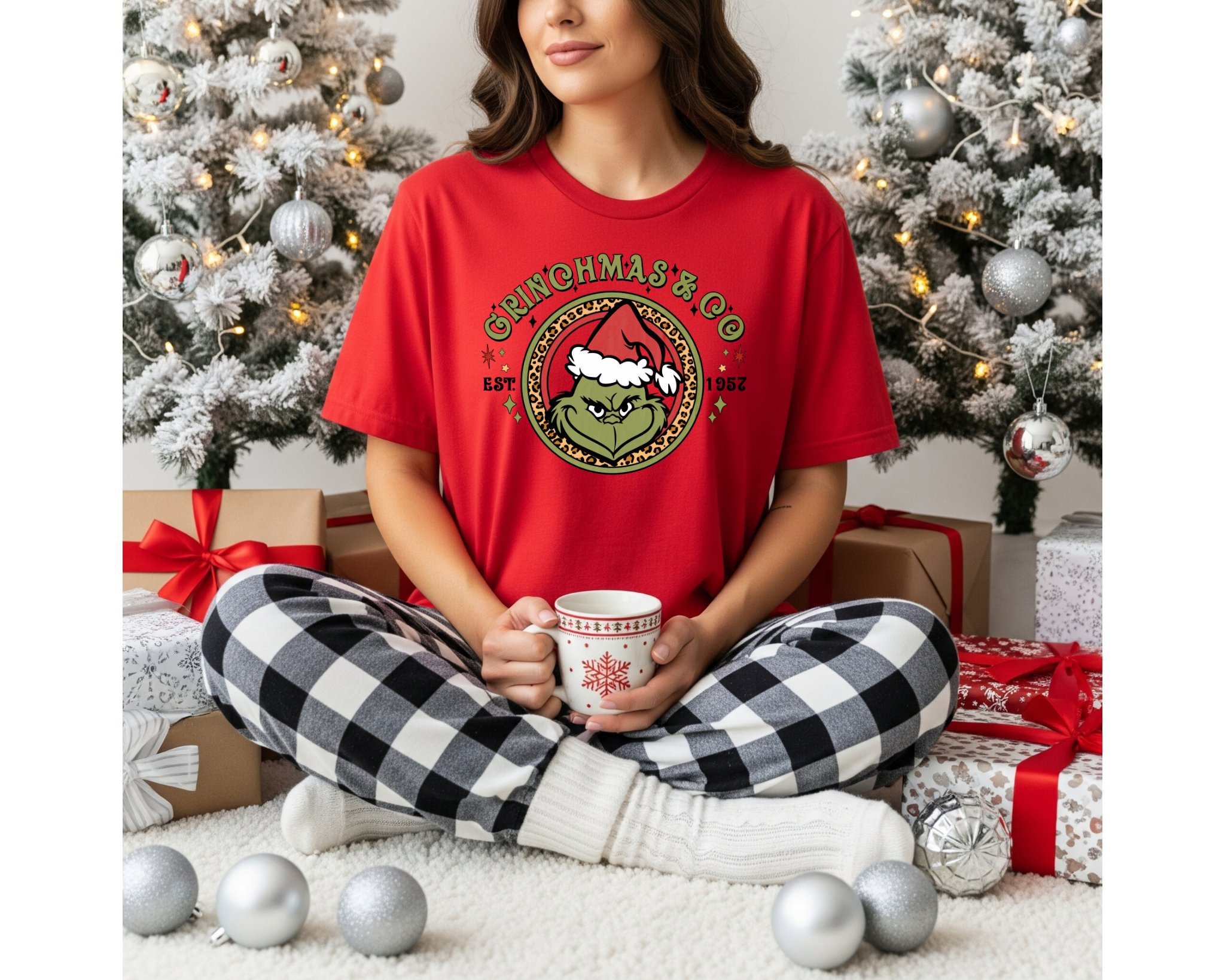 An adult wearing a red t-shirt with a “Grinchmas & Co.” holiday design featuring a Santa hat graphic, styled for festive Christmas gatherings.