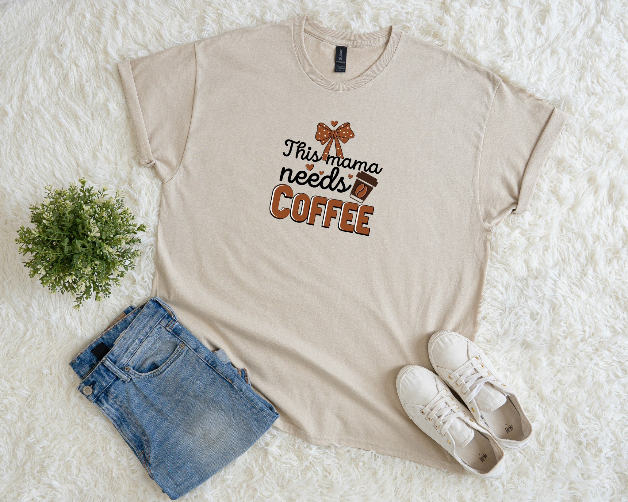 Beige t-shirt with 'This mama needs coffee' text, blue shorts, and white sneakers on a white surface.