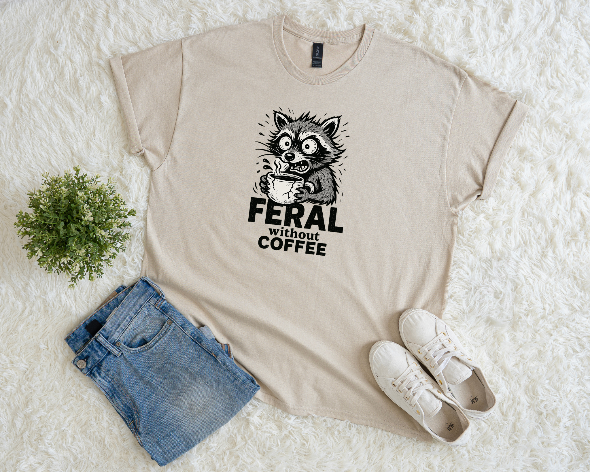 Beige t-shirt with a graphic design and text, paired with denim shorts and white sneakers on a textured white surface.