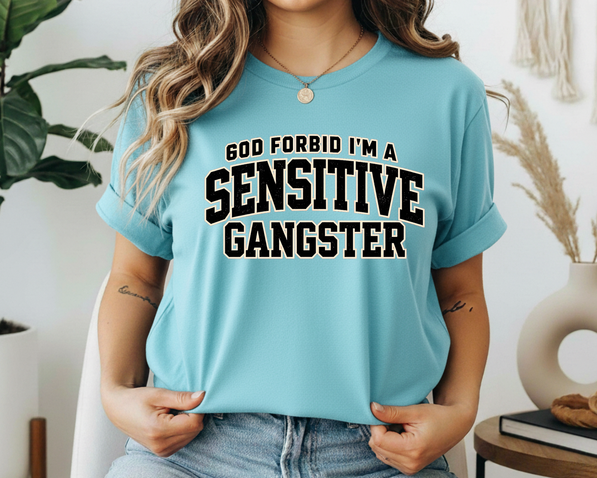 Person wearing a light blue t-shirt with text 'GOD FORBID I'M A SENSITIVE GANGSTER' in a casual setting.