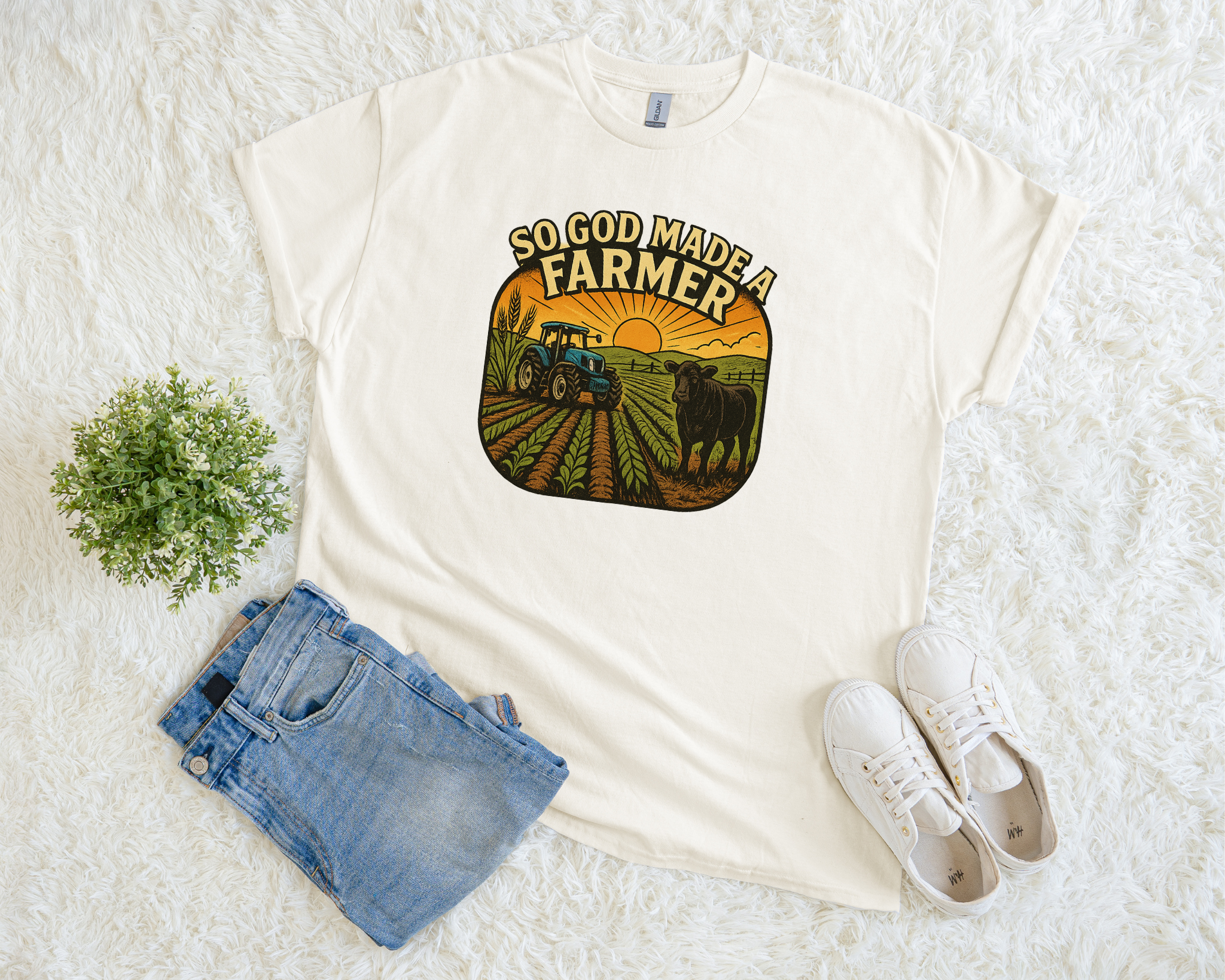 White t-shirt with a 'God Made a Farmer' graphic on a white surface with jeans and sneakers.