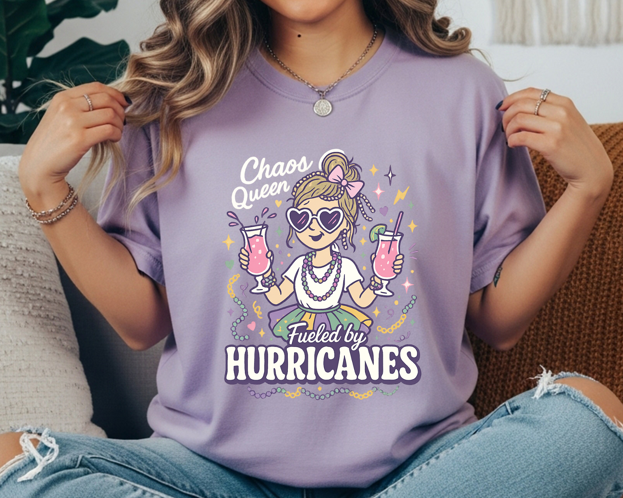 VIOLET Comfort Colors Mardi Gras t-shirt with a playful girl holding two pink hurricane drinks, surrounded by beads and sparkles, and the text “Chaos Queen Fueled by Hurricanes