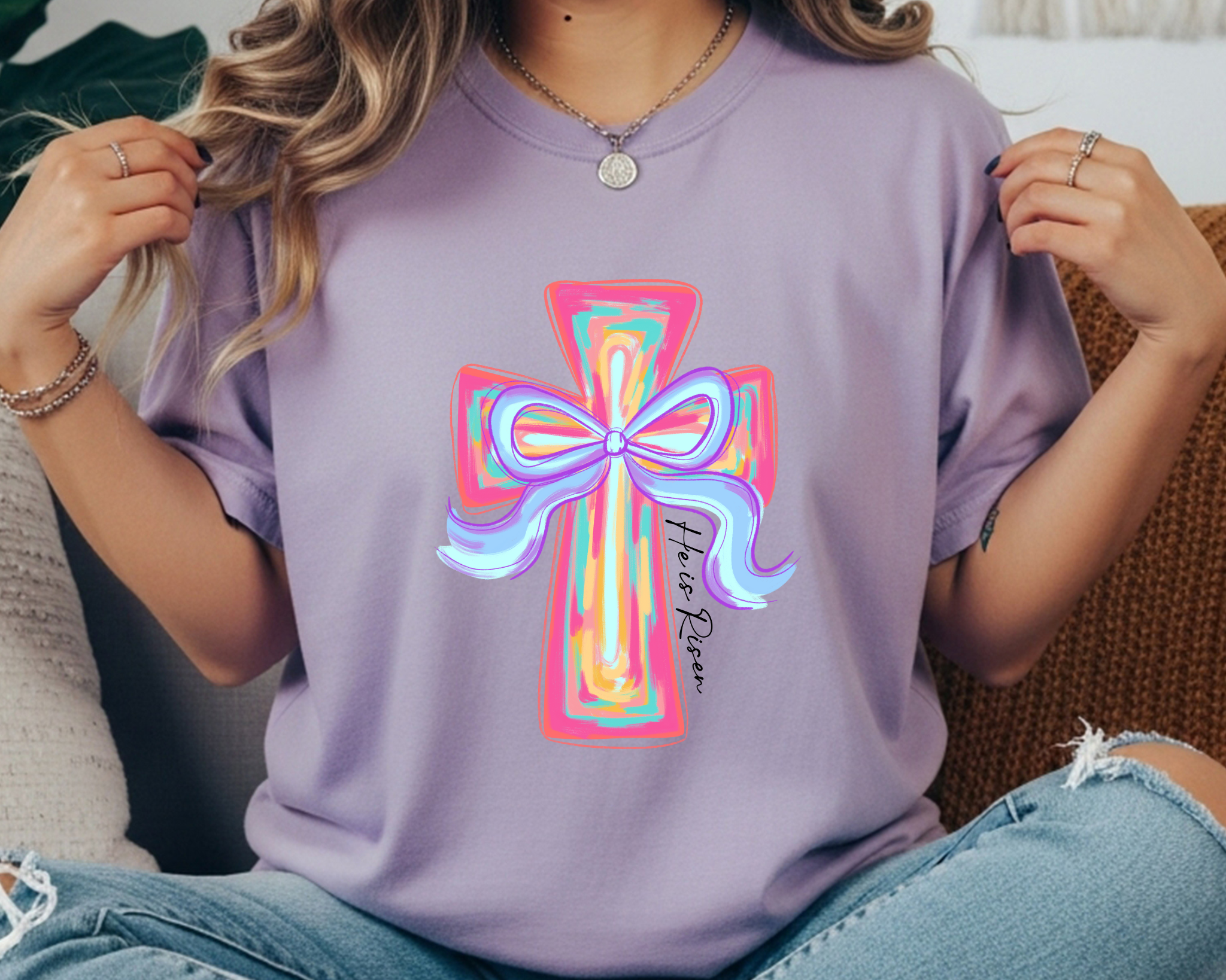 Comfort Colors t-shirt featuring a colorful pastel cross with a bow and “He Is Risen” script printed vertically along the cross.