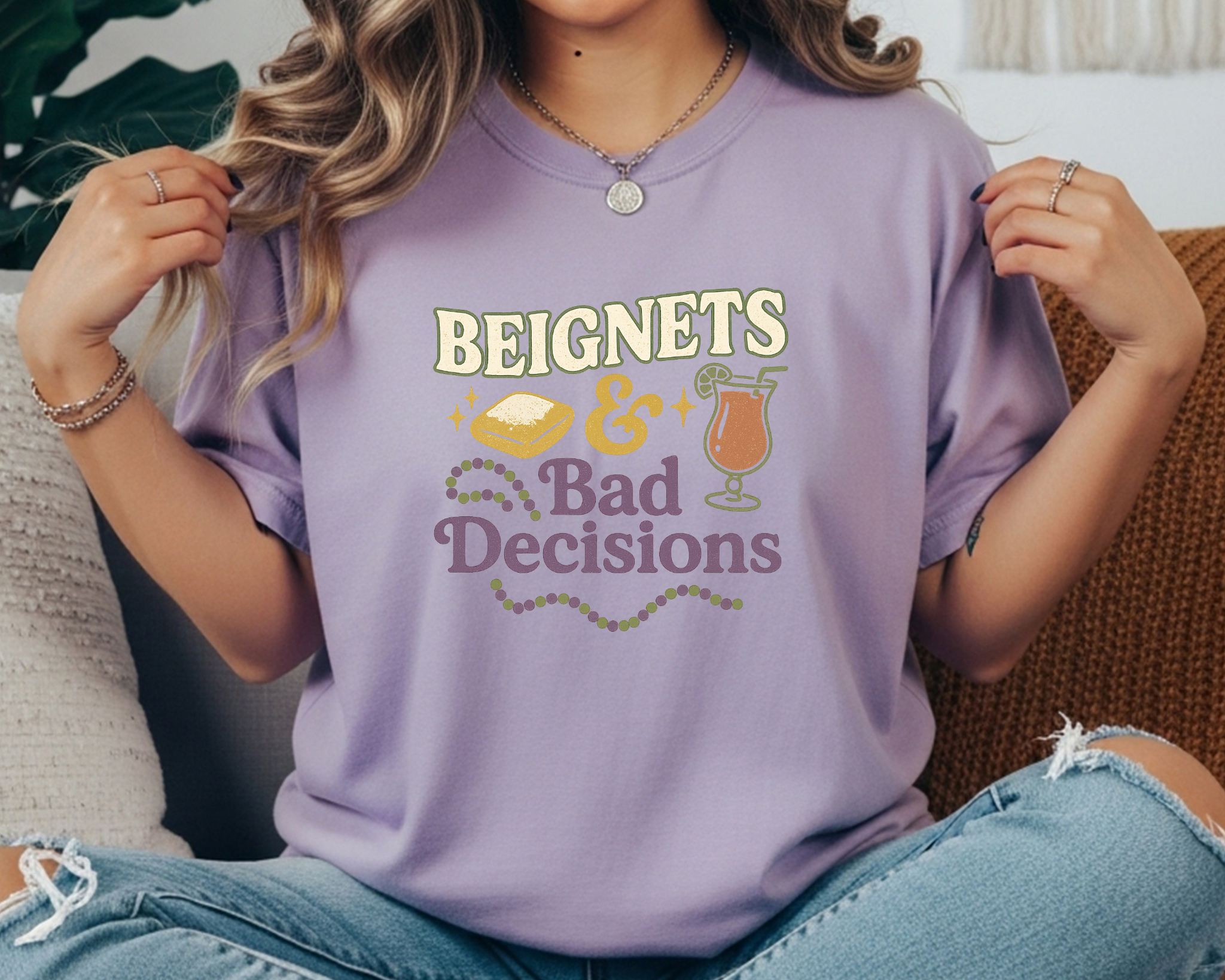 violet Comfort Colors tee with Mardi Gras design featuring beignet, cocktail, and text reading “Beignets & Bad Decisions” in purple, gold, and green.