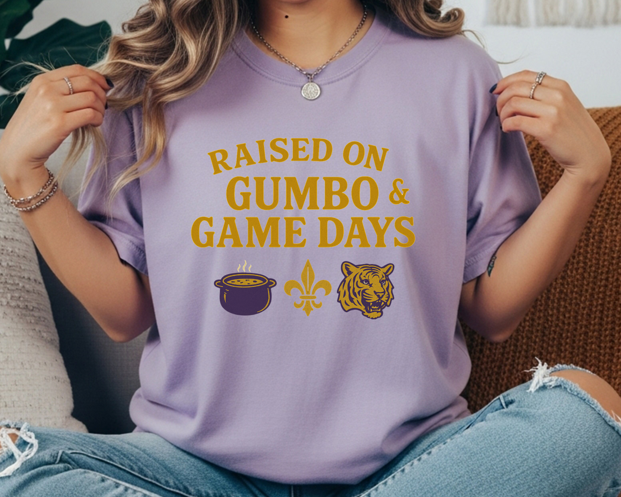 violet Comfort Colors tee with “Raised on Gumbo & Game Days” text and icons of a gumbo pot, fleur-de-lis, and tiger in gold and purple.