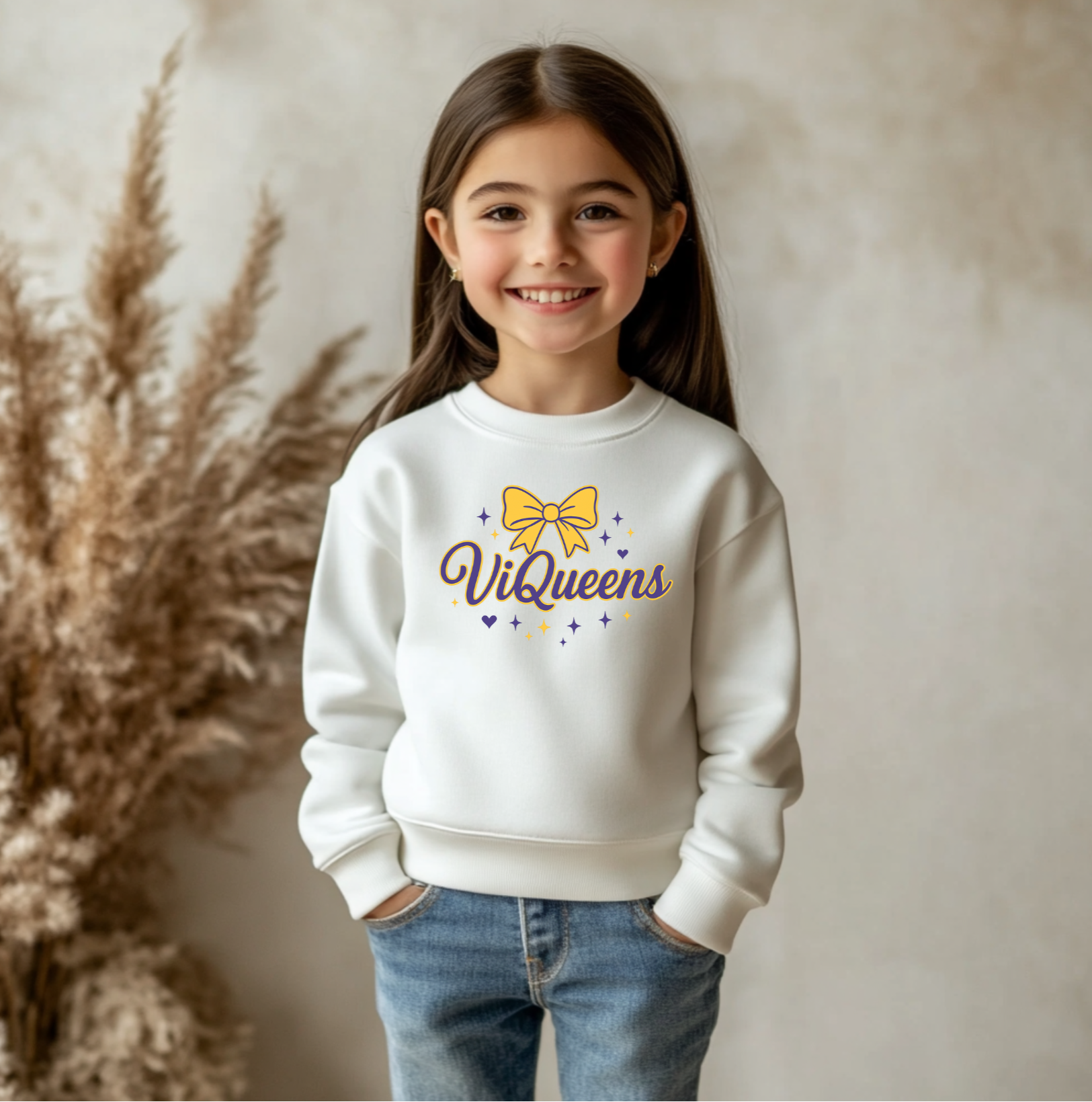 Young girl wearing a white sweatshirt with 'ViQueens' design, standing against a neutral background.