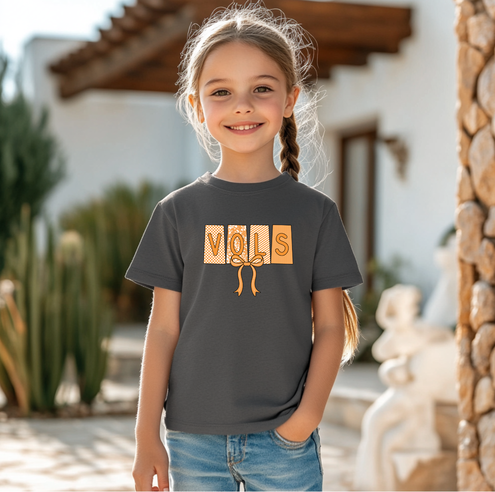 Young girl wearing a dark gray t-shirt with 'VOLS' printed on it, standing outdoors.