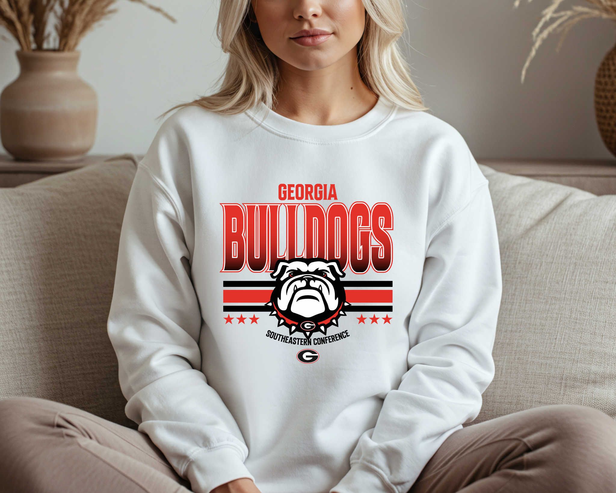 A woman wearing a Georgia Bulldogs-inspired crewneck sweatshirt featuring bold red and black graphics with a fierce bulldog design, sitting comfortably on a couch.