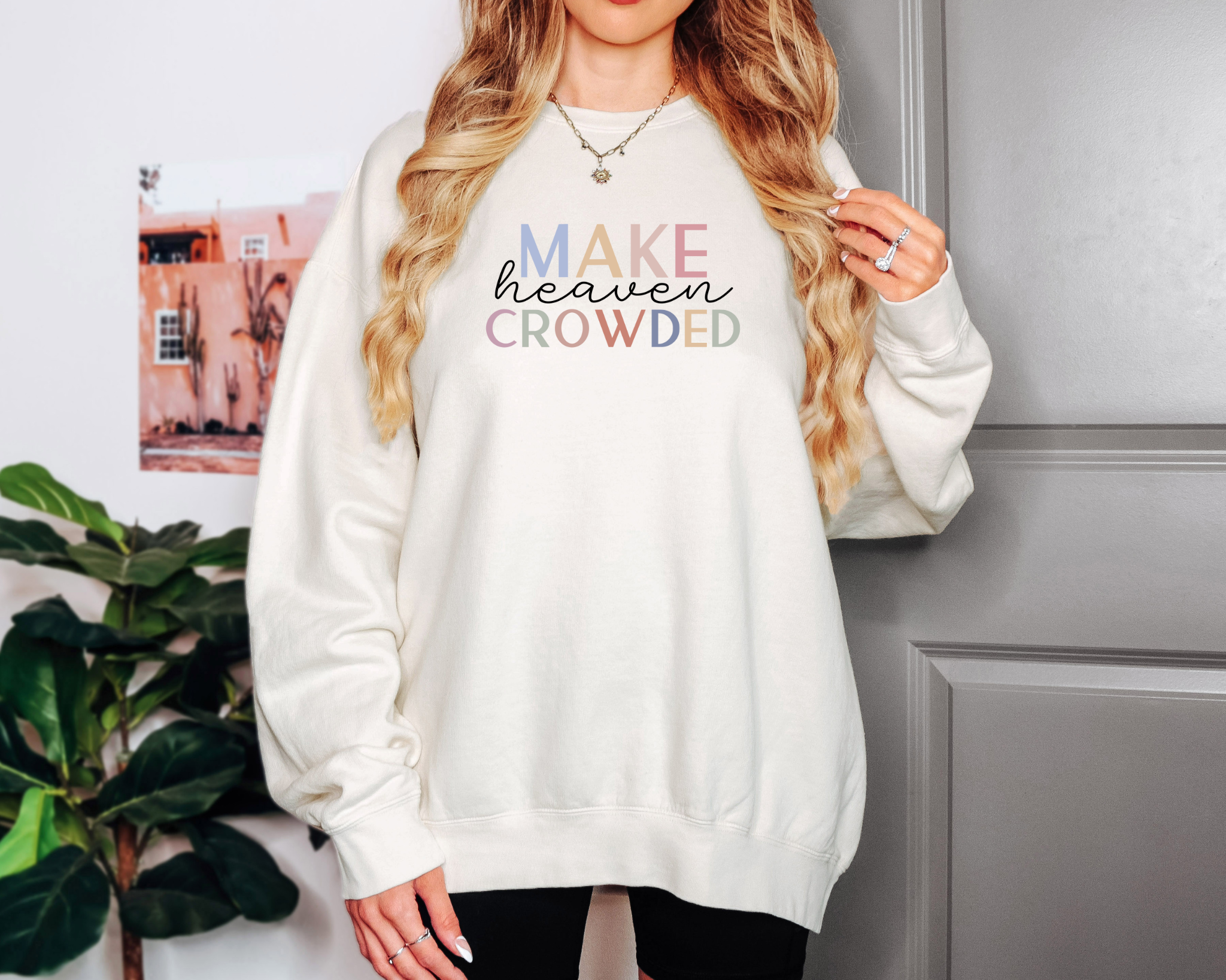 Woman wearing Make Heaven Crowded Comfort Colors Christian sweatshirt in bright pink, styled casually with jeans and layered jewelry.