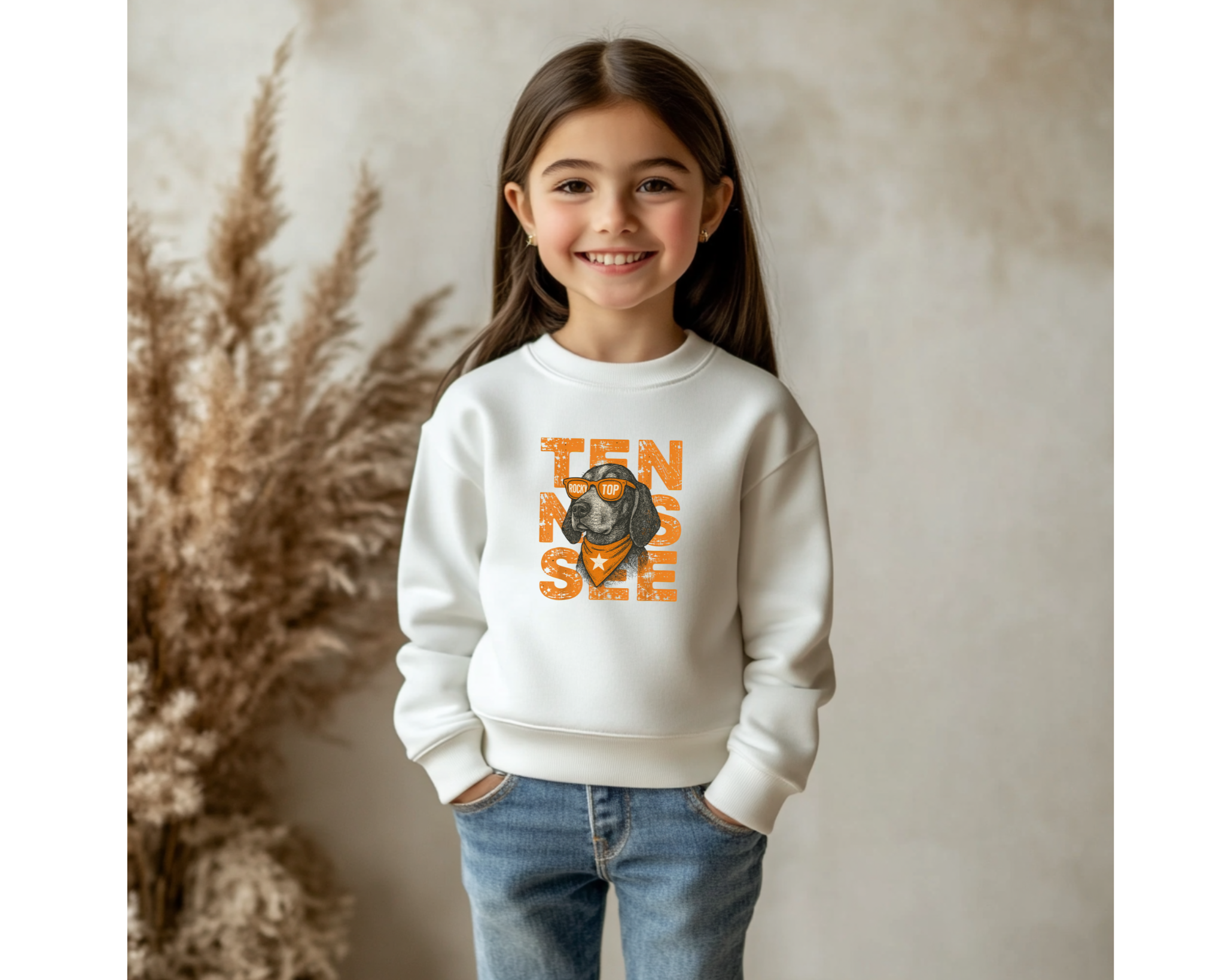 Child wearing a white sweatshirt with a vols smokey graphic and text, standing against a neutral background.